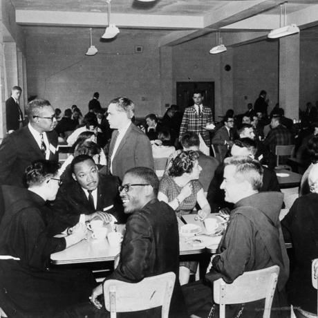 Martin Luther King Jr. seated in busy dining hall