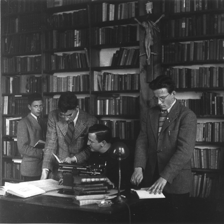 men around desk consulting books in library