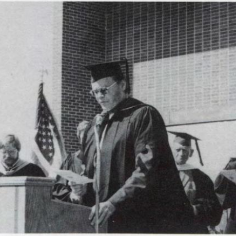 Ben Fink speaking at podium in front of the library, St. Francis College Graduation 1975