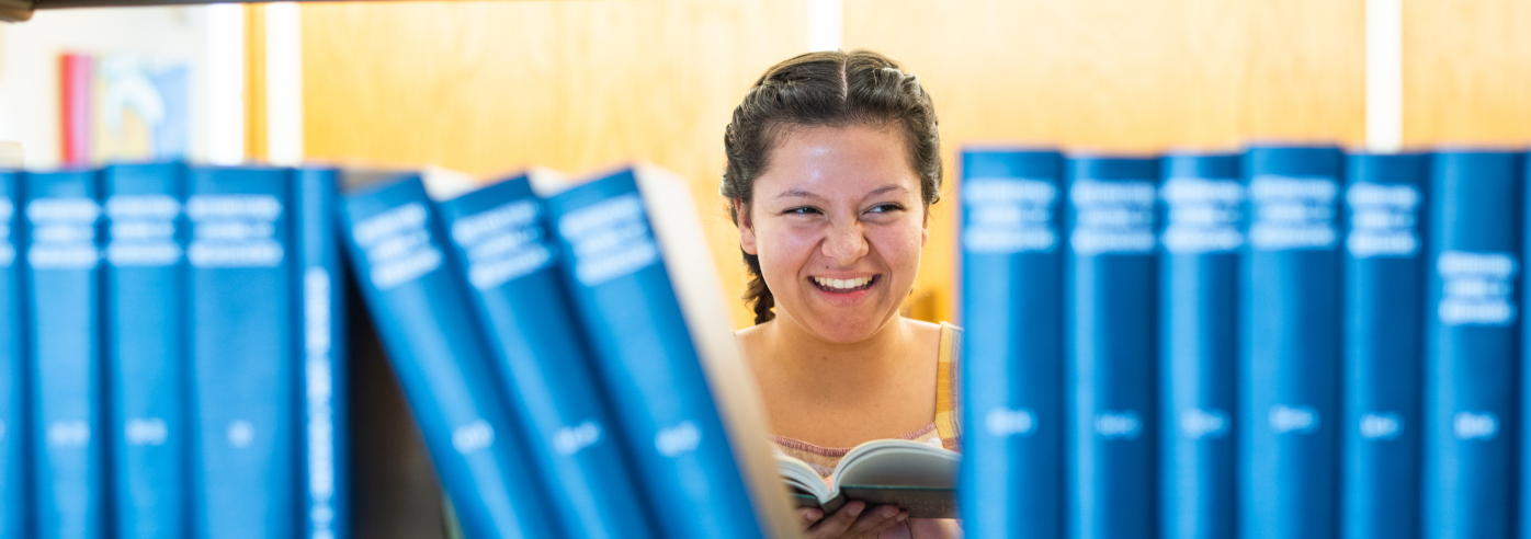 woman holding book and smiling as seen through bookshelf